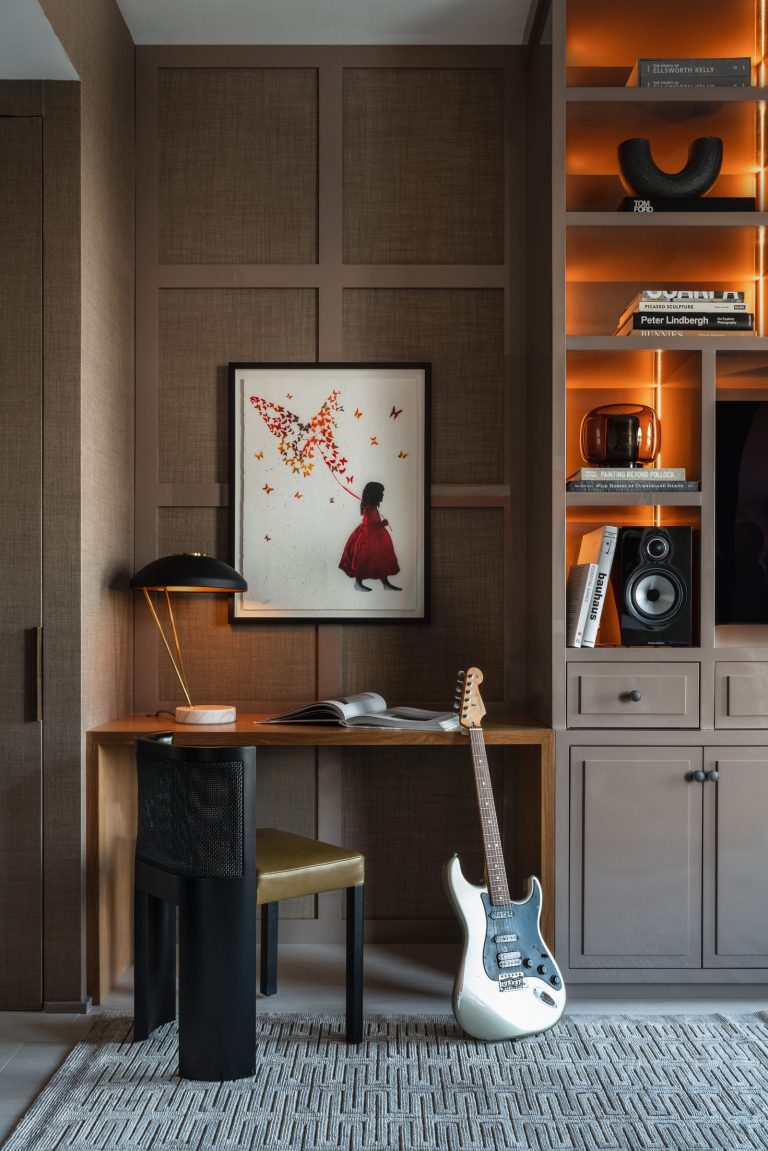 A cozy study nook with a wooden desk and black lamp is featured. A white electric guitar leans against the desk. A framed artwork of a girl catching butterflies hangs on the wall. Built-in shelves with books, decor, and a speaker are on the right. A textured rug covers the floor.